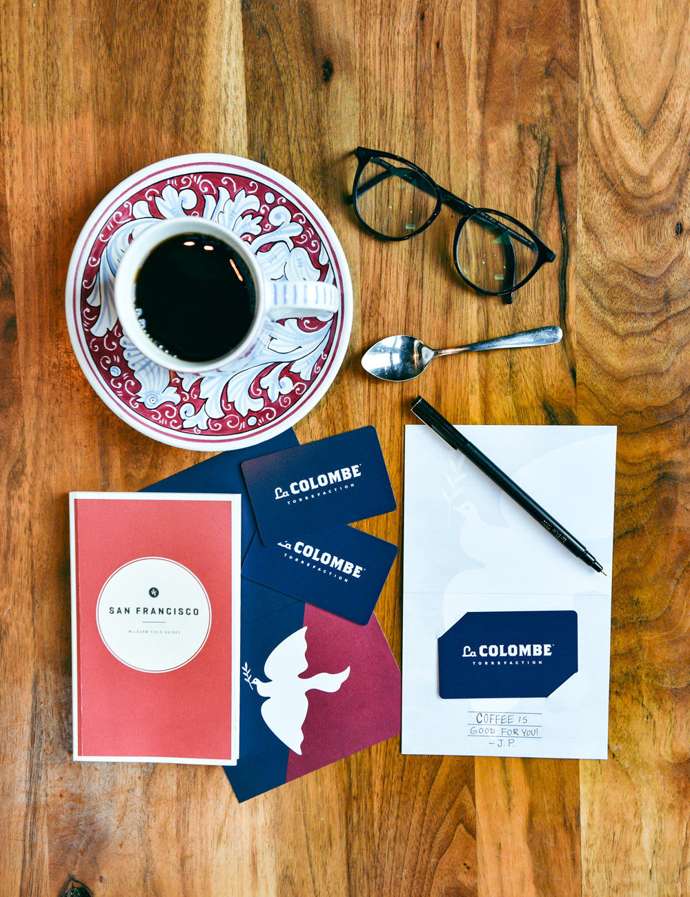Top view of several La Colombe Gift Cards with a cup of coffee, a card, and a pair of glasses.